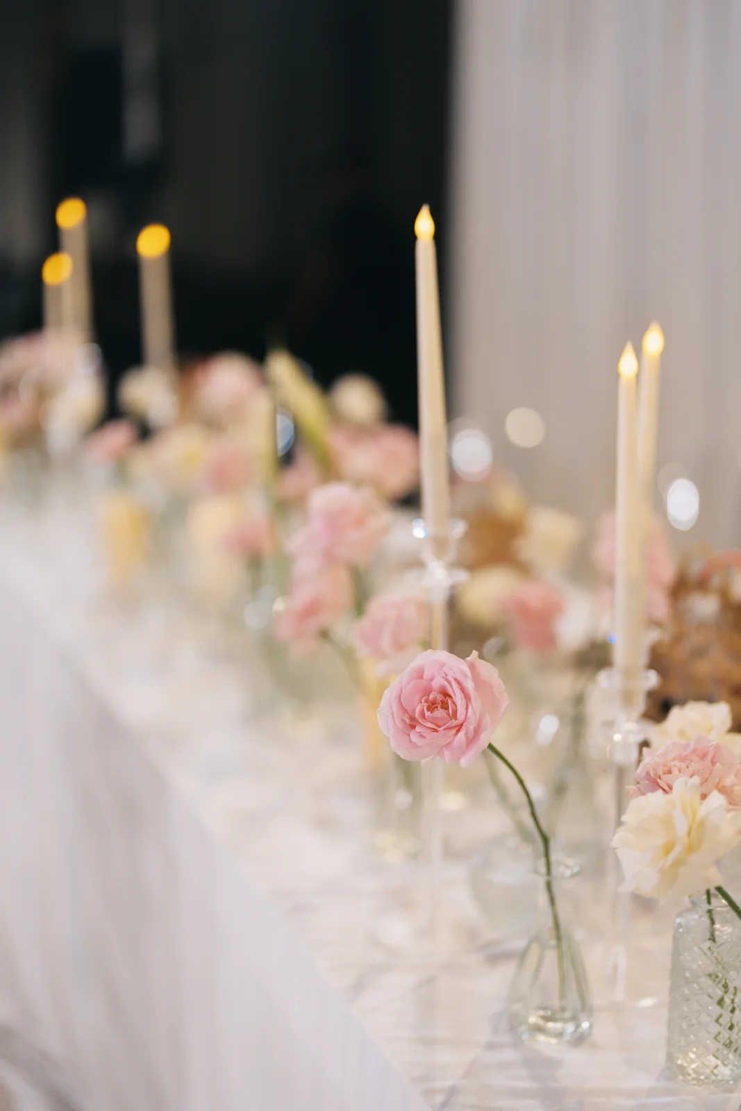 Blush roses, glass candleholders and white linen in a VANARA wedding table setting